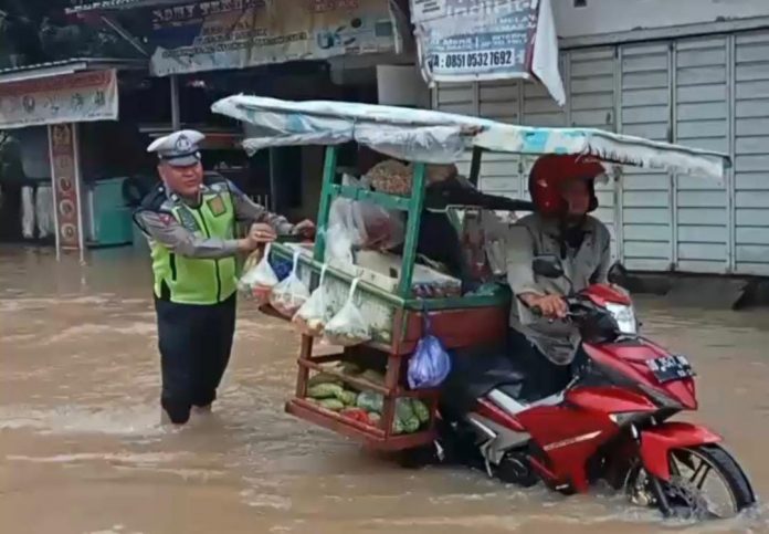 FOTO: Aiptu Nasir anggota Ditlantas Polda Sulsel berjibaku bersama pedagang sayur saat terjebak banjir di jalan trans nasional Sulawesi Selatan.