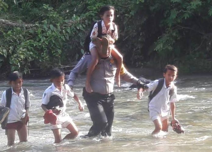 FOTO: Aipda Ismet Ishak saat membantu para pelajar menyeberangi sungai di wilayah pelosok di provinsi Gorontalo. (Properti via Google)
